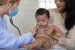 © Natee Meepian - Pediatrician using stethoscope on baby held by mother during check-up.