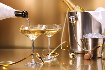 Canvas Print - Pouring champagne into glass against golden background, closeup