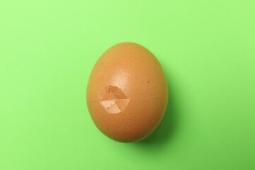 Wall Mural - One egg with cracked shell on green background, top view