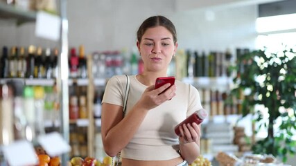 Wall Mural - Young woman buyer scanning qr code for red smoothie in bottle in grocery store 