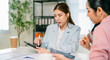 © Leny Studio - A woman in a light blazer uses a tablet while discussing with colleagues in a modern workspace, emphasizing teamwork and collaboration.