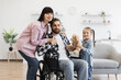 © sofiko14 - Caucasian family with father in wheelchair interacting warmly with mother and young daughter. Modern kitchen creates welcoming atmosphere. Captures family love, support, and disability awareness.
