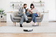 © sofiko14 - Caucasian parents and daughter on sofa using tablet with robot vacuum cleaner in living room. Modern technology and family time