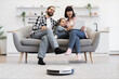 © sofiko14 - Caucasian parents and daughter on sofa using tablet with robot vacuum cleaner in living room. Modern technology and family time