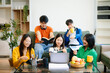 © laddawan - Group of young Asian students working on a project with laptops and tablets. Cozy indoor setting, teamwork,