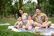 © Prathankarnpap - Happy asian parents with their two kids enjoying a weekend picnic in green park