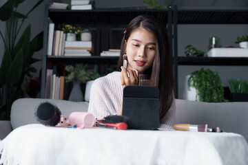 Wall Mural - Asian woman sits on sofa putting on makeup in living room