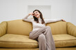 © Westend61 - Smiling young woman sitting on sofa in front of white wall