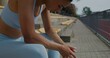 © m-art - A woman in sports clothes and with earbuds in her ears rests after a workout, sitting in the stands of the city stadium on a summer day