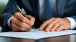 © Wilasini - Close up view of a businessman s hands signing a formal contract with financial graphs spreadsheets and documents spread across a desk representing a new investment partnership or business deal