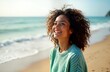 © Vadym - Joyful young woman smiles happily on sandy beach. Enjoys sunshine. Relaxing moment on vacation. Curly hair, wears light teal sweater. Summer day. Good mood. Positive emotional state. Perfect