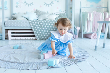 Sticker - Happy Little girl in dress is playing on floor with wooden cubes. Baby curly hair plays with toys in child room. Little girl plays in kindergarten. Child development. Cute child build with blocks. 