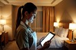 © Vadym - Hotel maid uses tablet in well-lit hotel room at night. Professional employee in uniform works, checks, manages tasks in modern tech way. Hospitality staff uses digital device in interior. Modern