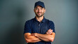 © Vadym - Pro male worker stands confidently with arms crossed. Wears navy blue polo shirt, hat. Backdrop plain gray. Image evokes sense of reliability, service. Could represent delivery driver, service