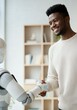 © Anna - African American man smiling while shaking hands with AI humanoid robot in modern office space
