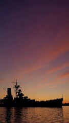 Poster - A dramatic silhouette of a battleship against a vibrant sunset, the harbor’s calm waters mirroring the golden hues of the sky.
 water.