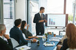 © peopleimages.com - Business man, presentation and monitor in office with group for b2b strategy, speech and graphs. Person, speaker and information on whiteboard, screen and sales with meeting for brand communication