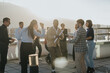 © qunica.com - A group of multiracial business colleagues is seen enjoying a celebration at sunset. They are dancing and socializing on a high-rise balcony, symbolizing success and teamwork in a relaxed corporate