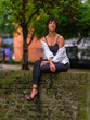 © Jesus-Salas-Dual - A young woman with curly hair sits on a brick wall near a set of stairs in an urban park. Wearing a black outfit with a white shirt, she gazes at the camera with a confident pose