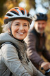 © Inspire Shots Hub - Senior woman with a helmet and jacket smiling while cycling outdoors, showcasing an active lifestyle, joy of cycling, and connection with nature alongside a companion