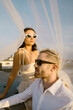 © Maskot - Young married couple wearing sunglasses while sitting under veil on rooftop