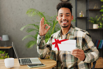 Sticker - Young smiling man he wear casual clothes hold gift certificate coupon voucher card for store show ok okay sitting alone at table in coffee shop cafe relax rest in restaurant during free time indoors.