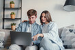 © Daniel - Happy millennial couple sit relax on couch in living room watching video on laptop together, smiling young husband and wife rest on sofa at home browsing Internet using modern computer device.