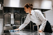 © Maskot - Low angle view of female chef cleaning kitchen counter in restaurant