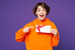 © ViDi Studio - Young smiling happy woman wear orange hoody casual clothes hold point finger on gift certificate coupon voucher card for store isolated on plain purple background studio portrait. Lifestyle concept.