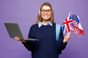 Wall Mural - Young smart girl IT student wear blue casual clothes glasses backpack bag hold flags use work on laptop pc computer isolated on plain pastel purple background. High school university college concept.