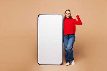 Wall Mural - Full body young fun woman she wear red casual clothes big huge blank screen mobile cell phone smartphone with area do winner gesture isolated on plain pastel light beige background. Lifestyle concept.