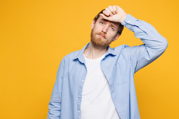 Young sad sick ill tired Caucasian man he wear blue shirt white t-shirt casual clothes put hand on forehead suffer from headache isolated on plain yellow background studio portrait. Lifestyle concept.