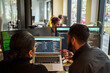 © Maskot - Rear view of male and female coding professional discussing over laptop while working in tech startup office