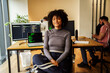 © Maskot - Portrait of curly haired female IT professional sitting in front of desktop PC at tech office