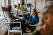 © Maskot - Smiling nurse talking with elderly man sitting on chair at care home