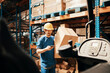 © Davor - Smiling male worker using smartphone and carrying box in large warehouse