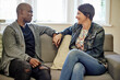 © peopleimages.com - Therapy, counseling and couple on sofa happy and talking in session for consulting, support and marriage. Psychology, interracial and black man and woman in conversation, discussion and communication