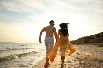 Wall Mural - Lovely couple running together on beach at sunset, back view