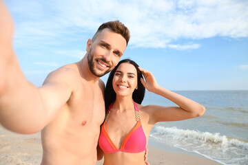 Wall Mural - Happy young couple taking selfie on beach