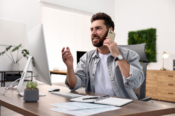 Wall Mural - Man talking on smartphone while working at table in office