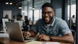 © Muqaddas - A smiling black man typing on a laptop in a modern office, working as a copywriter on a web project