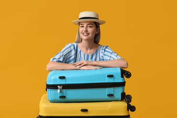 Wall Mural - Beautiful young woman with suitcases on yellow background. Travel concept