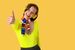 © Pixel-Shot - Young woman in headphones showing thumb-up on yellow background