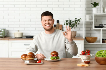 Wall Mural - Young man with tasty burgers showing OK in kitchen