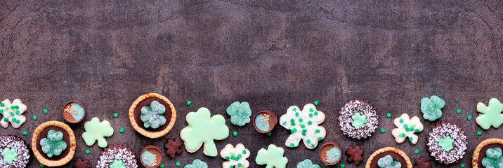 Aufkleber - St Patricks Day dessert bottom border over a dark stone banner background. Shamrock and green cookies, tarts, chocolate and candy. Top down view. Copy space.