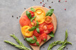 © Pixel-Shot - Wooden board with slices of different fresh tomatoes, basil, rosemary and peppercorn on grey background
