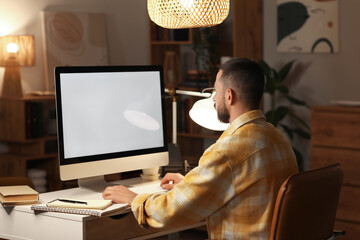 Wall Mural - Young man working with blank computer in office at night