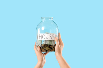 Wall Mural - Woman holding jar of money for house on blue background