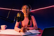 © InfiniteFlow - Smiling creative young beautiful Asian influencer talking in channel with positive podcast speech at night time, using laptop for presentation online at pink neon light modern studio. Stratagem.