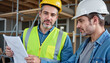 © Alina - Collaboration between two construction workers discussing blueprints at a building site